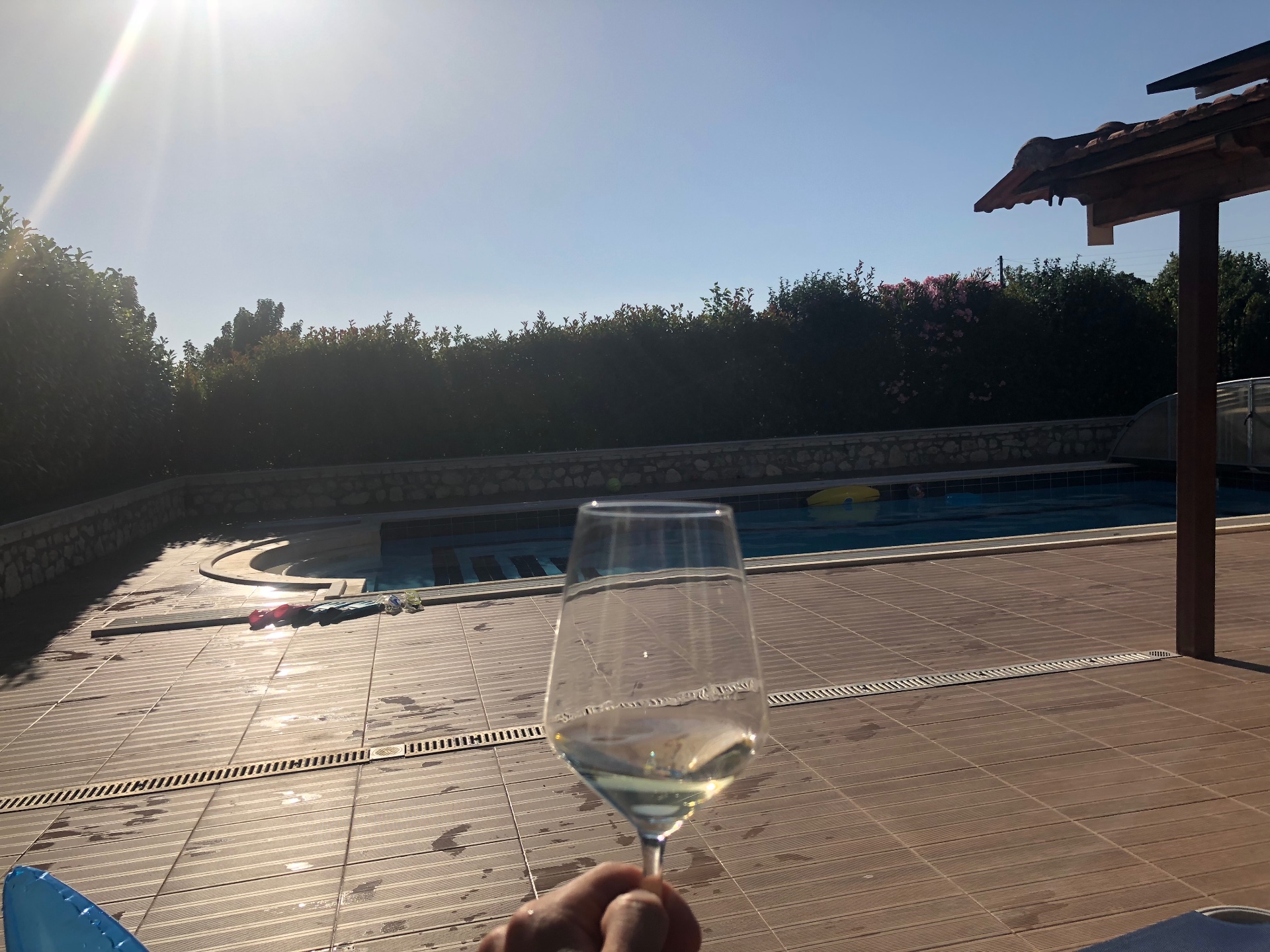A glass of chilled white wine held above the Villa Arcadia pool at golden hour
