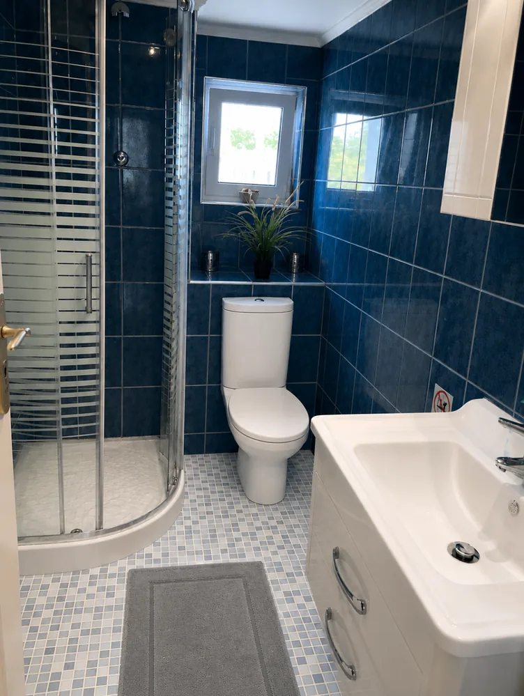 Blue-tiled bathroom with shower, sink and window at Villa Arcadia