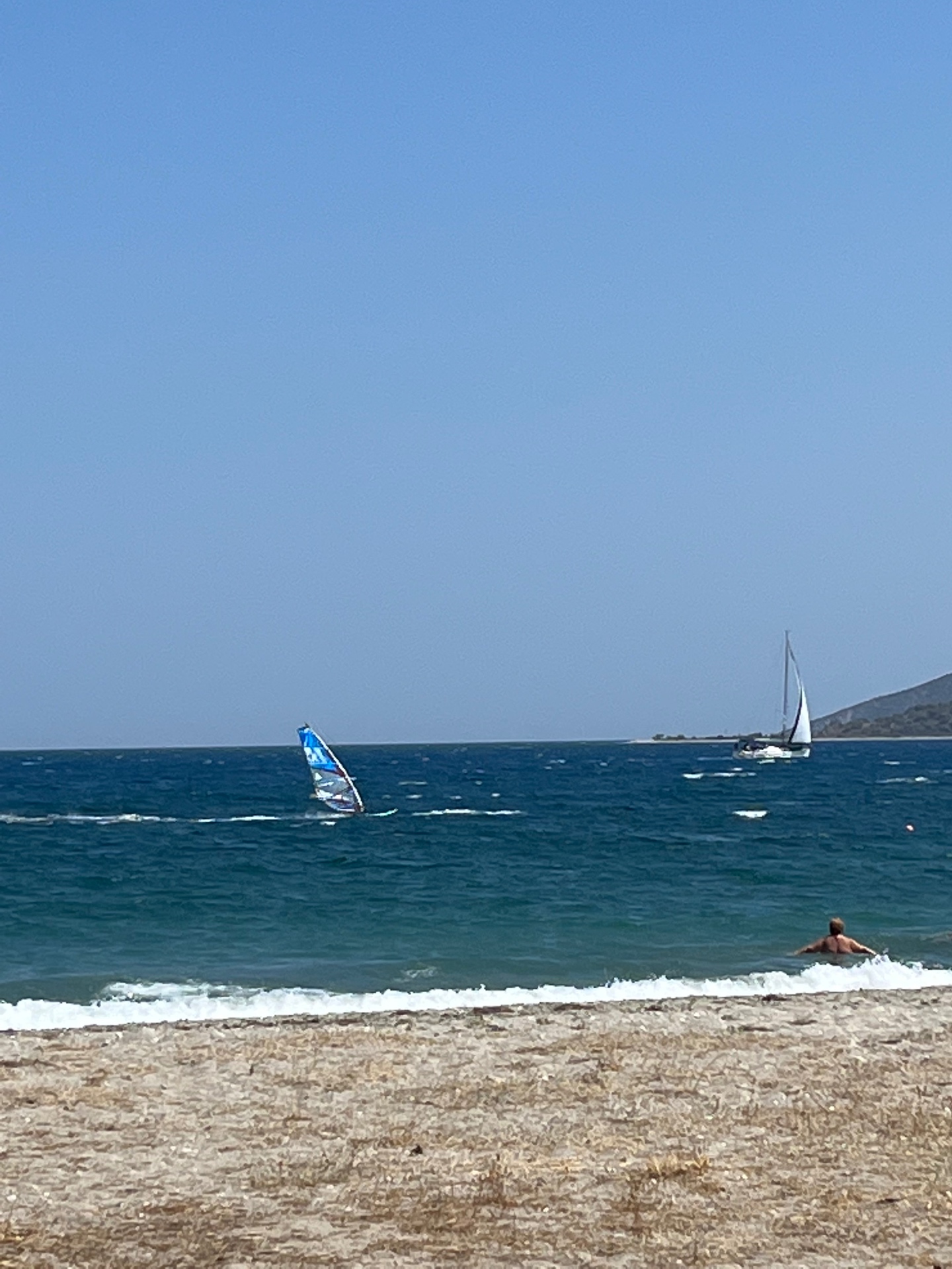 A windsurfer and a sailboat on the bay at Astros windsurf beach in the Peloponnese
