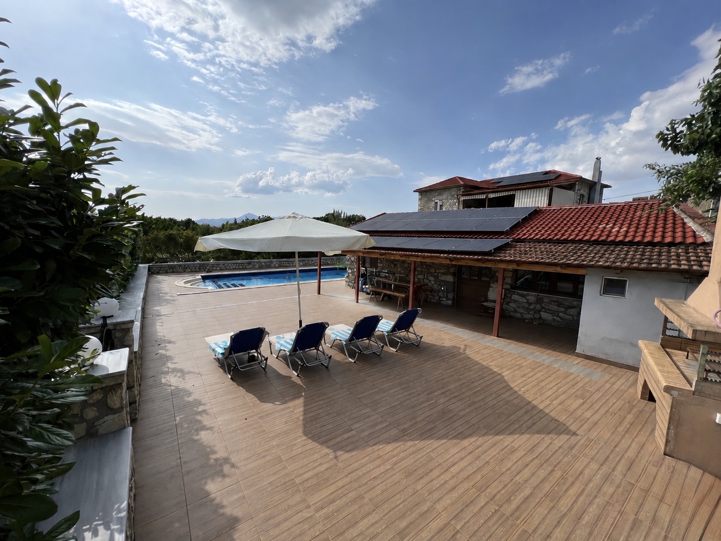 Large tiled pool terrace with sun loungers, parasol, outdoor kitchen and stone-built villa
