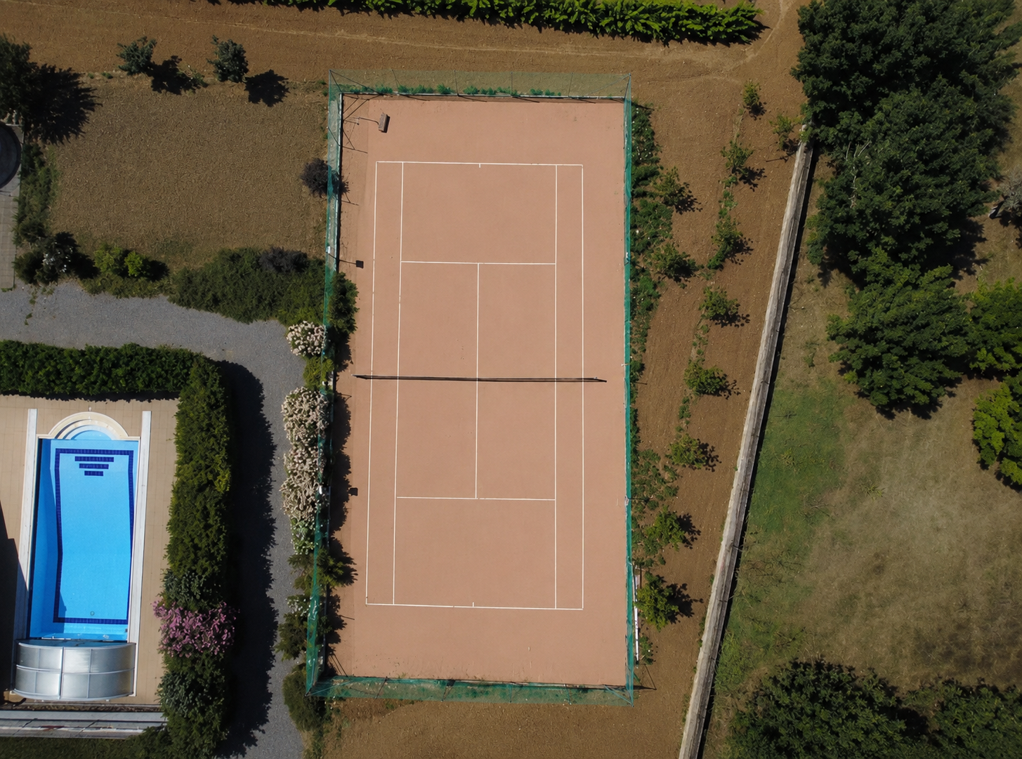 Overhead drone view of the private clay tennis court at Villa Arcadia next to the pool
