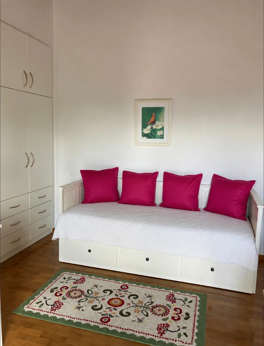 Guest room daybed with bright pink cushions and patterned rug at Villa Arcadia