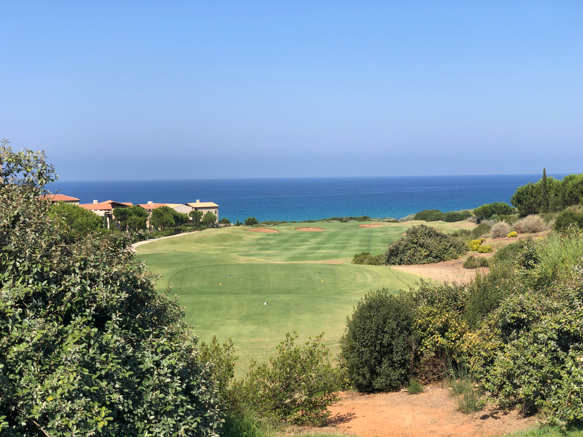 Costa Navarino fairway running down to the Ionian Sea with cliffside resort buildings