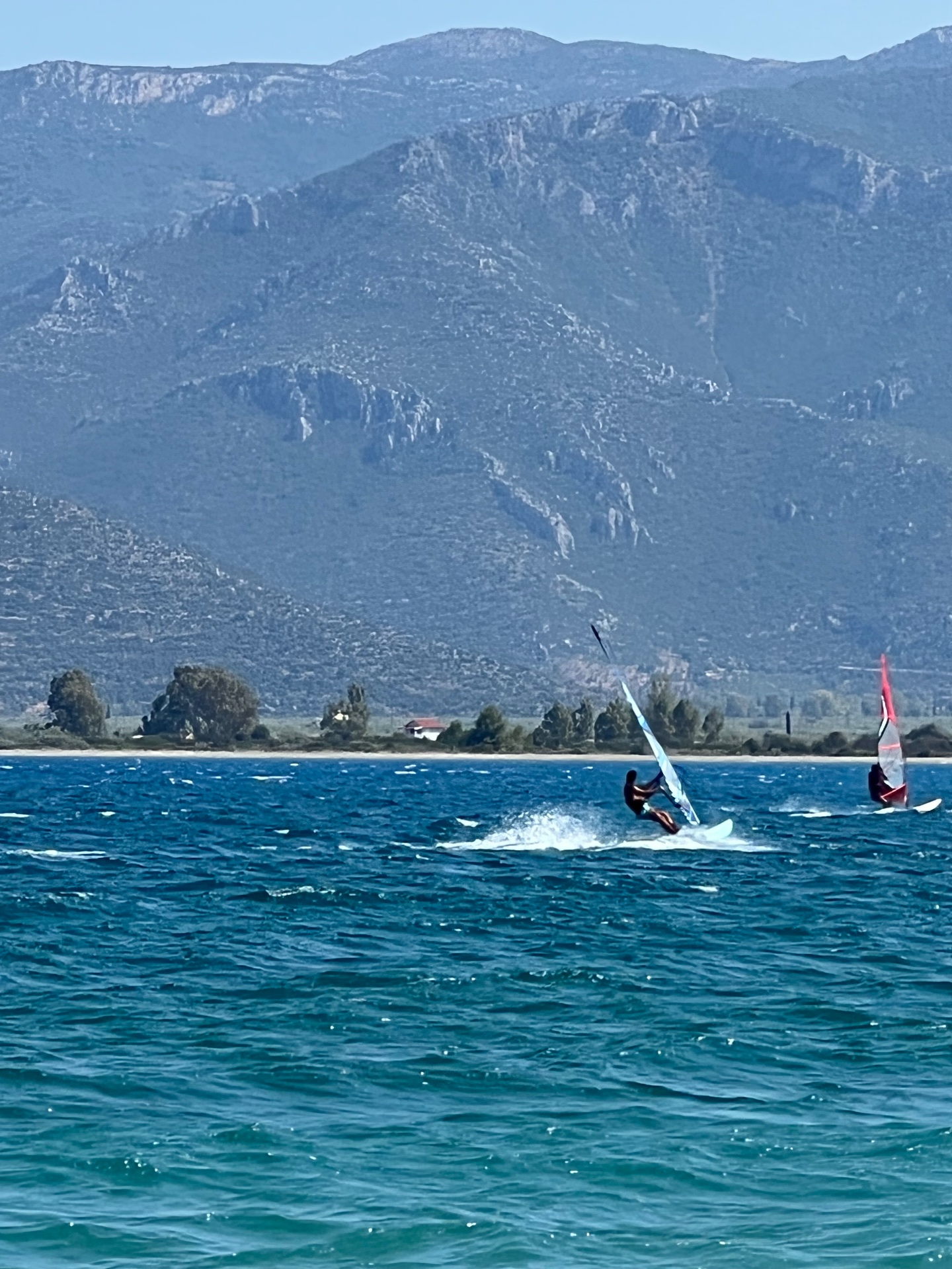Two windsurfers carving across the bay at Paralio Astros with the Parnon mountains behind