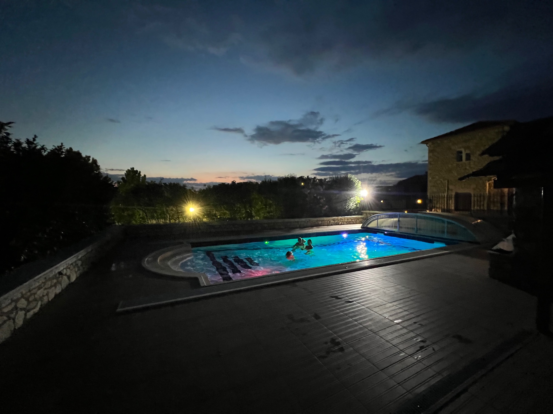 Villa Arcadia pool lit blue at night with guests swimming under a twilight sky
