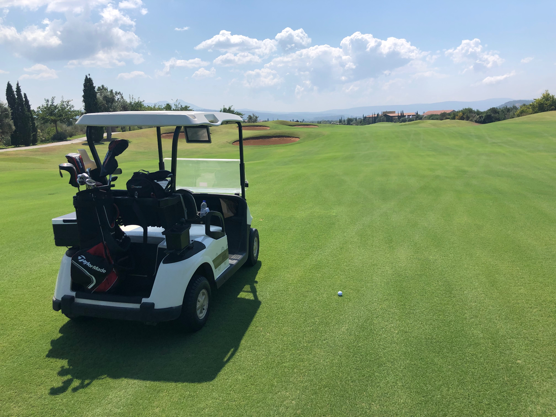 Golf buggy with clubs parked on a manicured fairway at Costa Navarino with Arcadian mountains behind